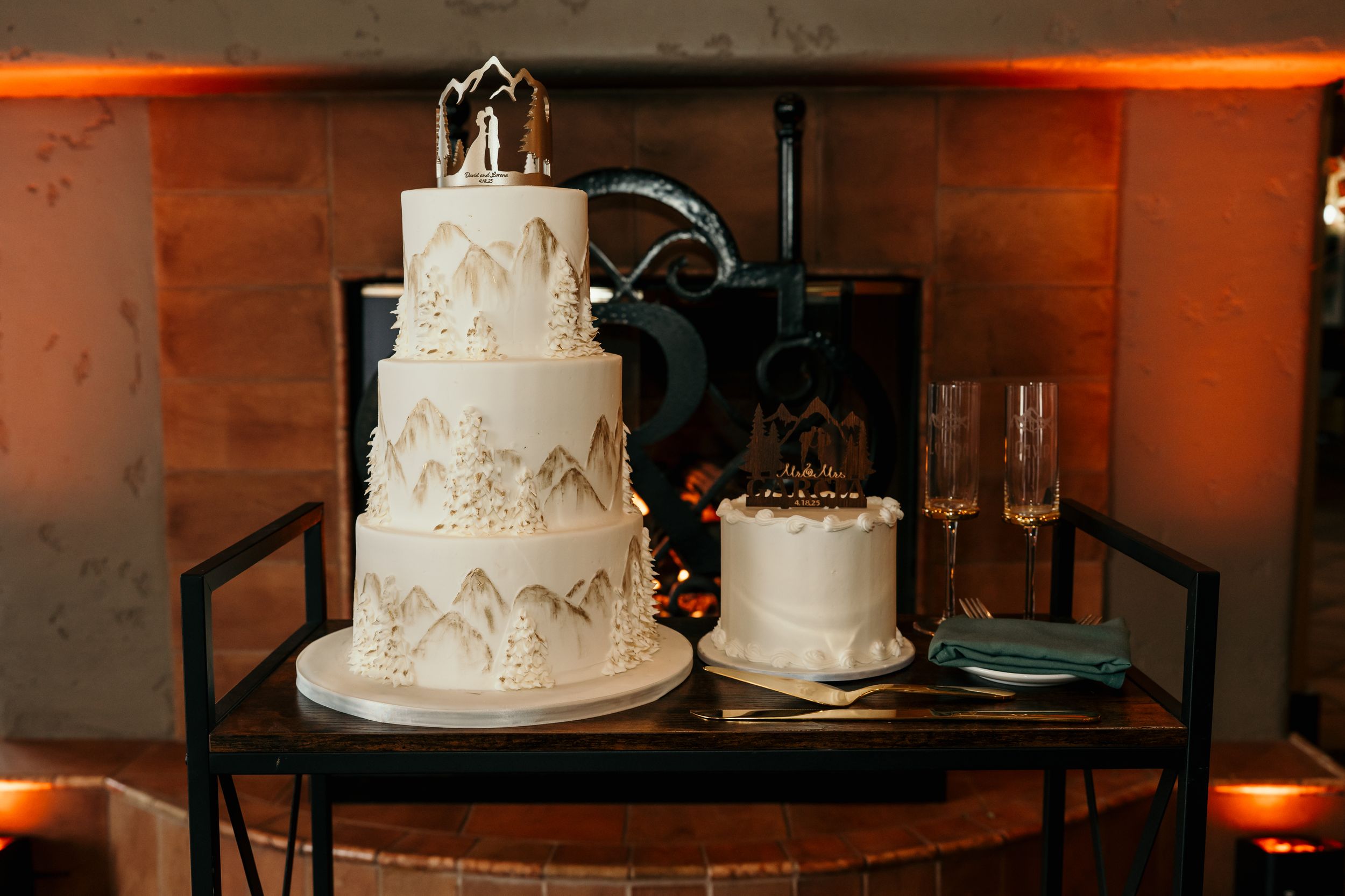 Three-tiered white wedding cake with intricate designs displayed against rustic brick wall with orange ambient lighting.