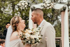 Romantic wedding couple embracing under a floral arch with mountain scenery.