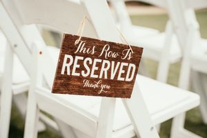 Wooden 'Reserved' signs on white chairs at an outdoor wedding ceremony.
