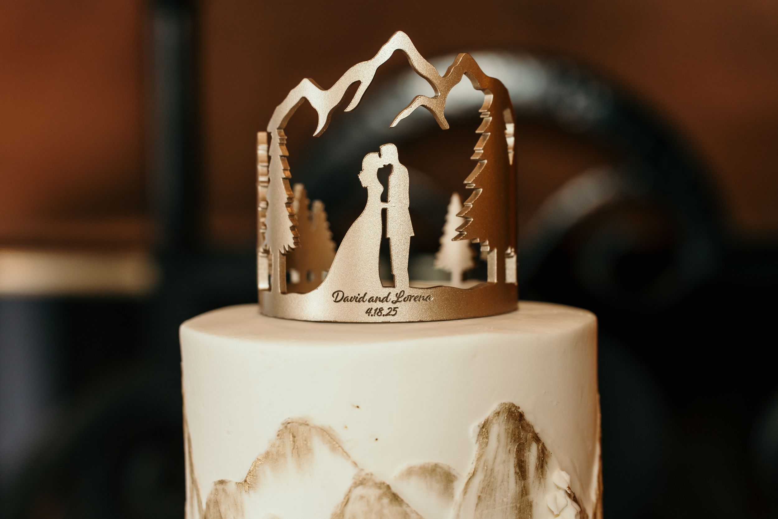 Elegant white wedding cake decorated with delicate lace patterns and a silhouette topper in warm lighting.