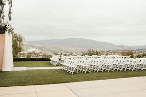 Rows of white folding chairs set up for an outdoor wedding ceremony with mountain views in the background.