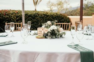 Elegant outdoor wedding reception tables decorated with white linens, greenery and string lights overhead.