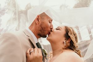 Romantic wedding couple embracing under flowing white veil with soft natural lighting.