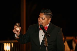 A speaker in formal attire raises a champagne glass during an evening toast.