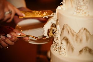 A wedding cake being cut with a silver knife while hands hold plates to serve the slices.