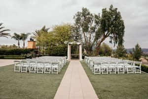 Outdoor wedding ceremony setup with white chairs and aisle runner leading to an altar space.