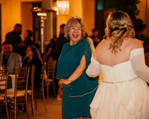 Joyful wedding celebration scene with guests and bride in white dress under warm venue lighting.