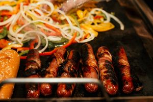 Grilled sausages and vegetables cooking on a dark metal grill surface.