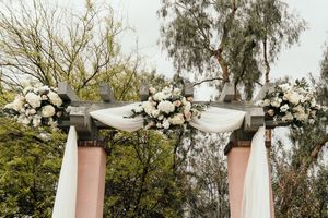 White fabric draped between pillars with floral arrangements creating an elegant outdoor ceremony space.