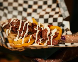 Close-up view of loaded sweet potato skins topped with meat and drizzled with white sauce on checkered paper.