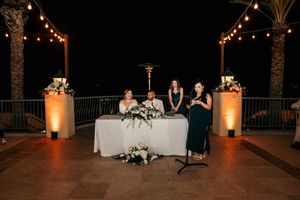 Wedding reception setup with elegant lighting and white floral arrangements on tables at night.