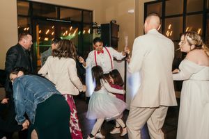 Wedding guests dancing and celebrating on a dimly lit indoor dance floor during evening reception.