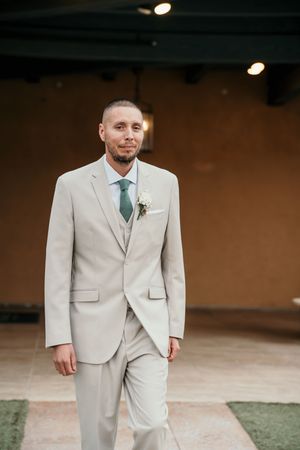 Groomsmen in light beige suits standing in a formal pose at an outdoor venue.
