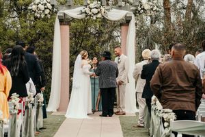 Outdoor wedding ceremony setup with white floral arrangements and guests gathering.