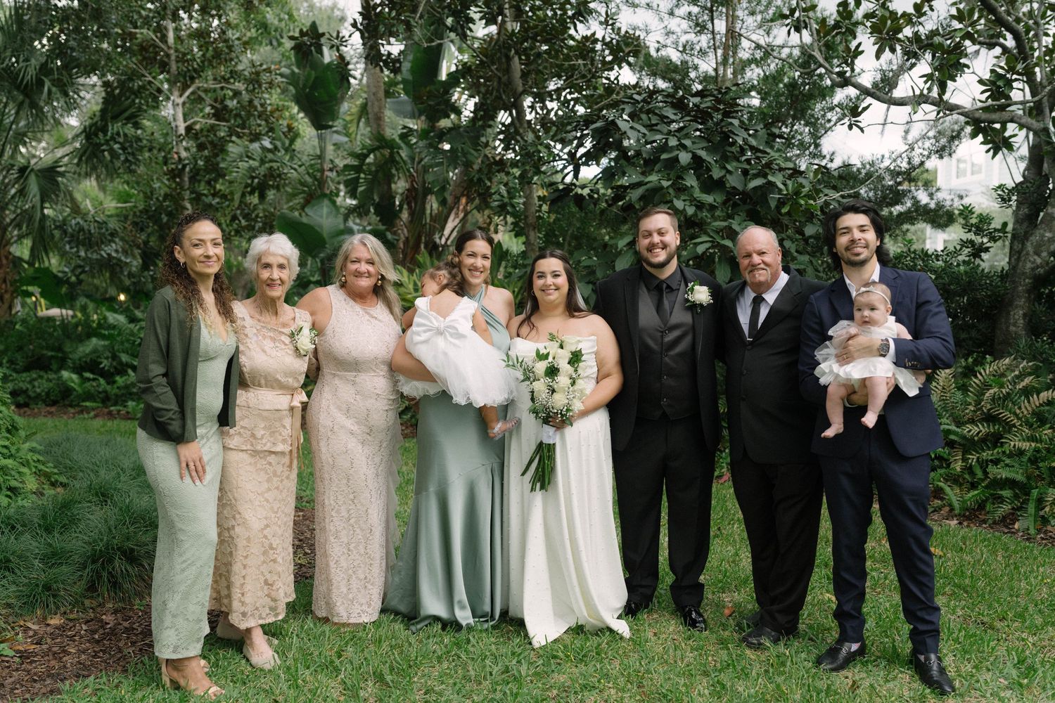Wedding party poses together in lush garden setting wearing coordinated champagne and neutral colored attire.