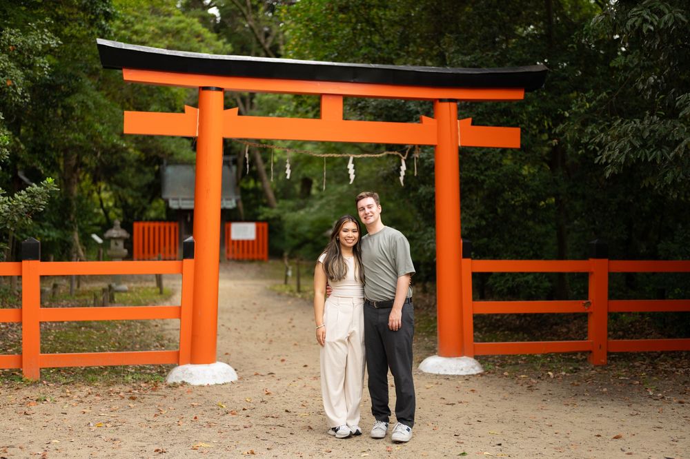 Couple smiling together under a traditional orange Japanese torii gate in a serene forest.