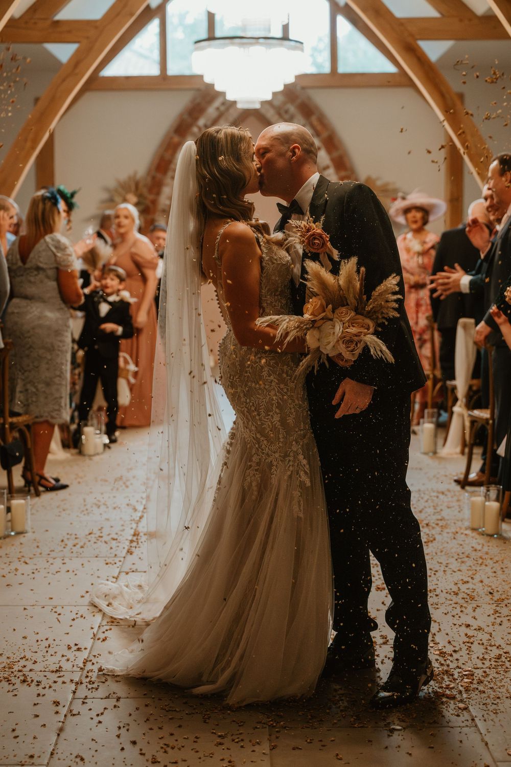 Wedding couple and guests celebrate on dance floor with confetti falling in rustic barn venue during reception.