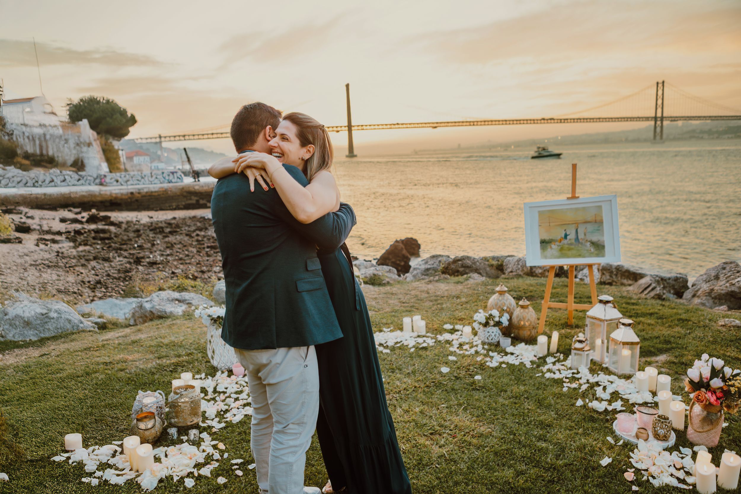 Intimate seaside celebration setup with candles and flowers at golden hour along rocky coastline.
