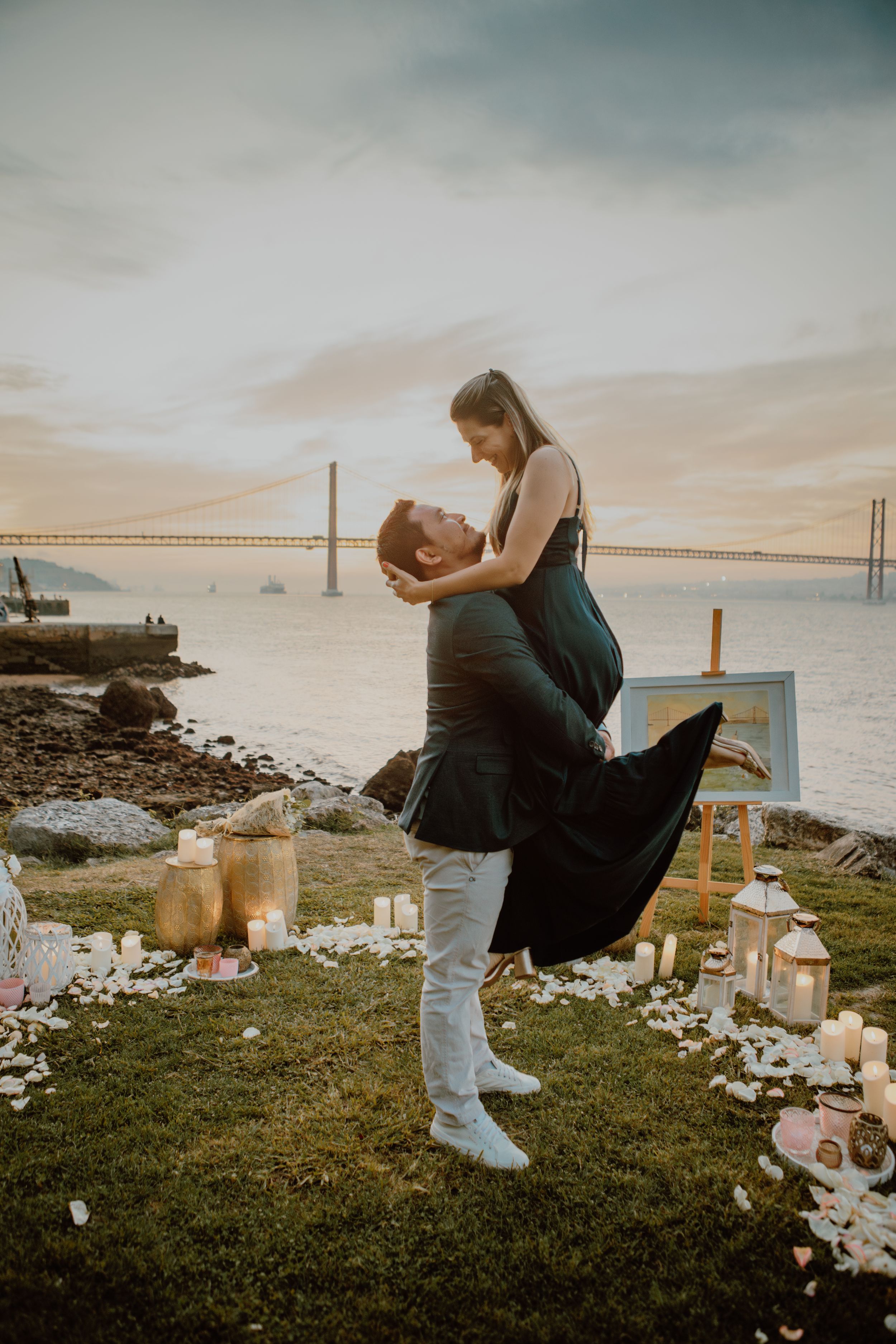 A couple embracing during a romantic sunset proposal by the ocean with candles and decorations.