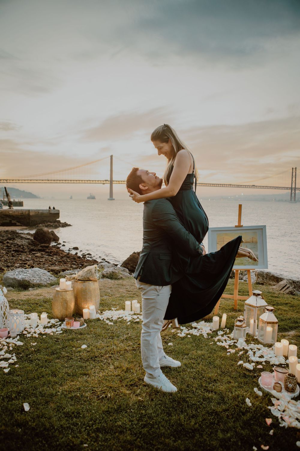 A couple embracing during a romantic sunset proposal by the ocean with candles and decorations.