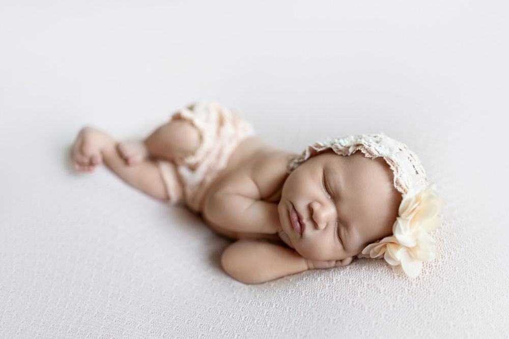 Newborn baby sleeping peacefully on soft white blanket with delicate lace headband.
