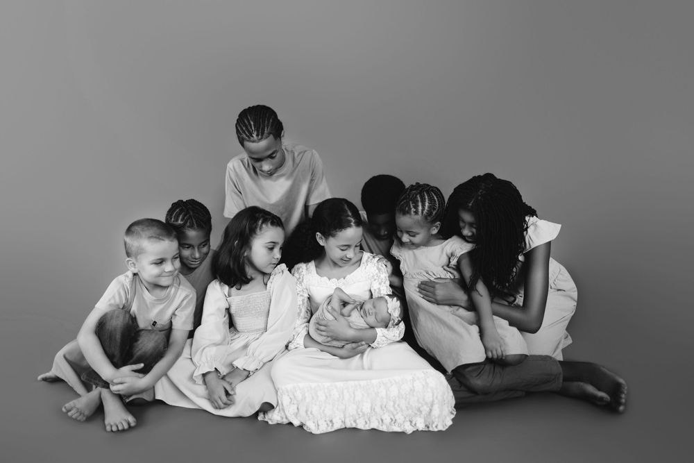 Black and white studio portrait of children sitting together in a row on the floor looking at a phone.