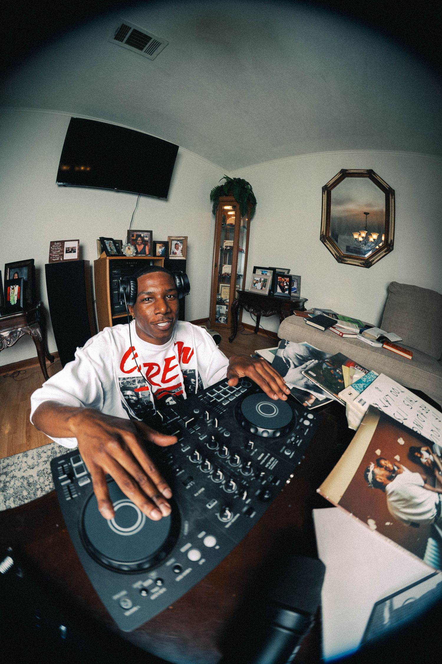 DJ wearing headphones operates turntable and mixer in home studio with fisheye lens effect.