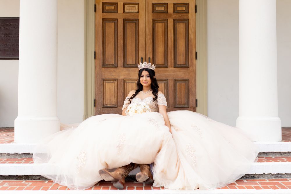 Bride in a flowing white gown sits gracefully on outdoor stairs with white columns in the background.