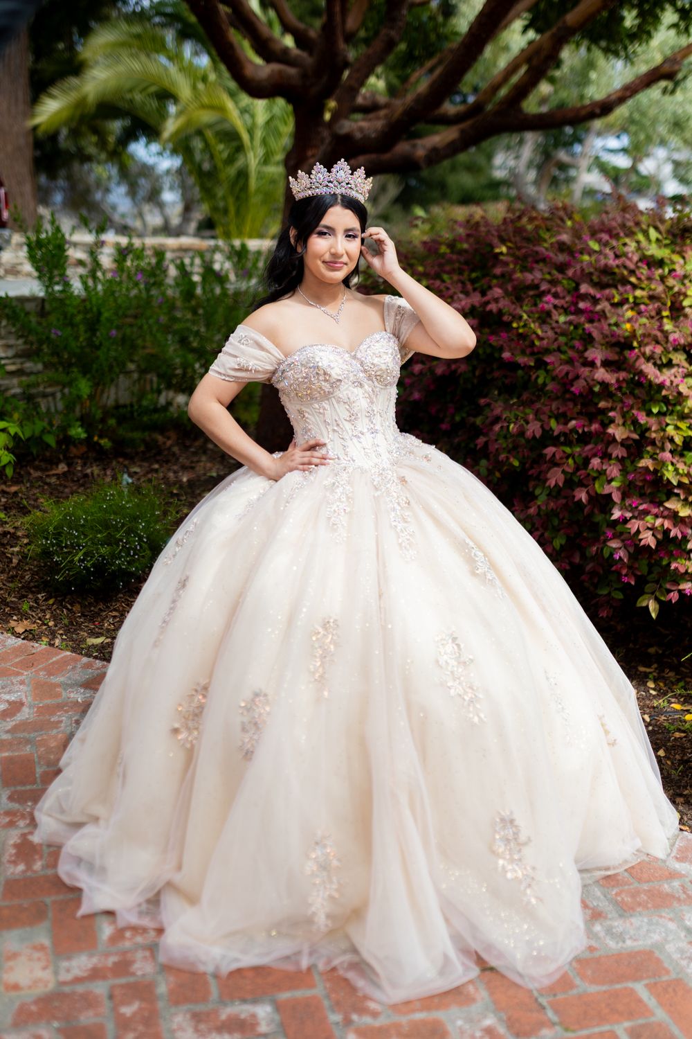 A stunning off-white ball gown wedding dress with delicate lace appliques and a crystal crown set in a garden setting.