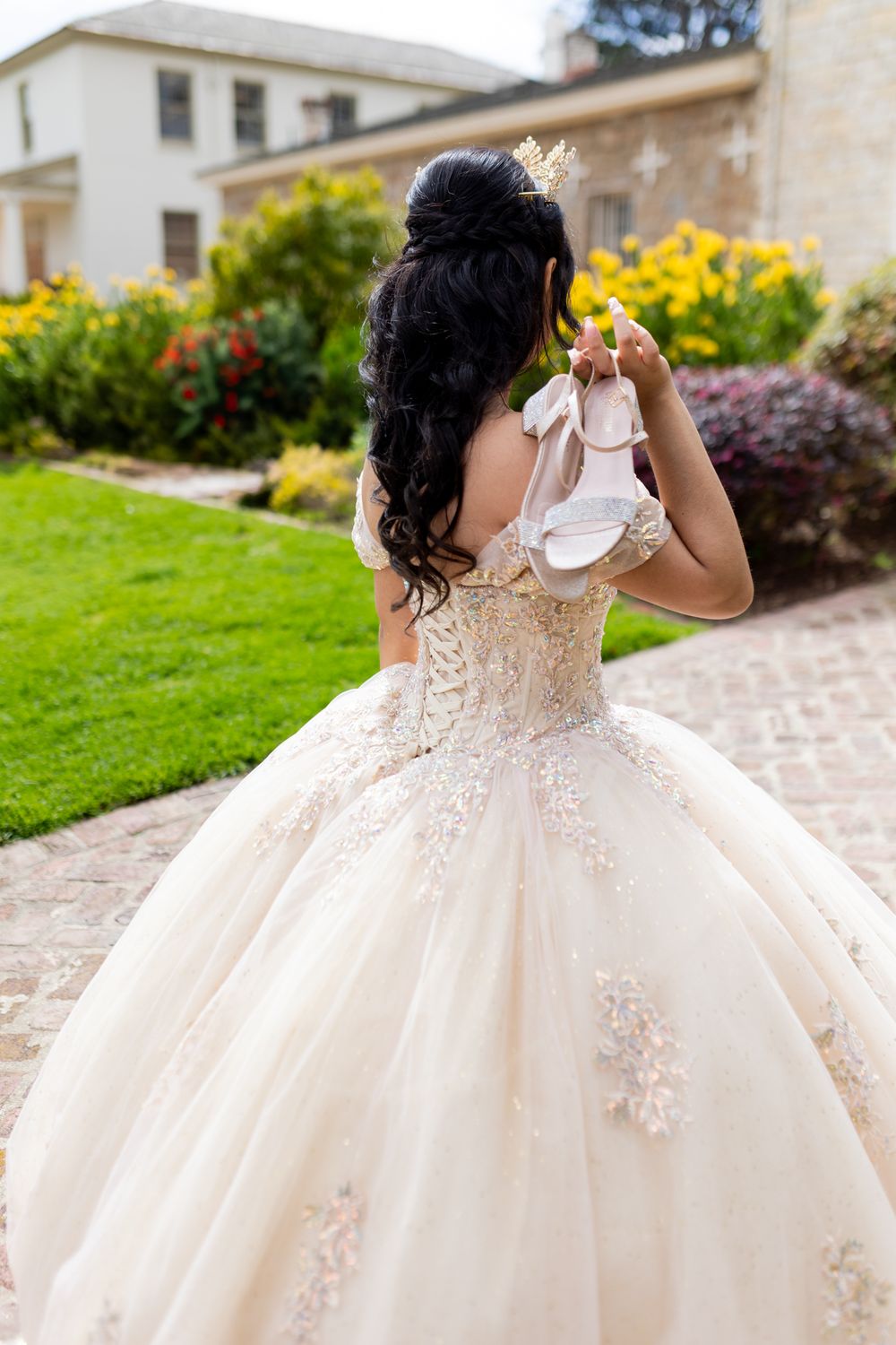 Back view of an ornate wedding dress with detailed corset and flowing tulle skirt in a garden setting.