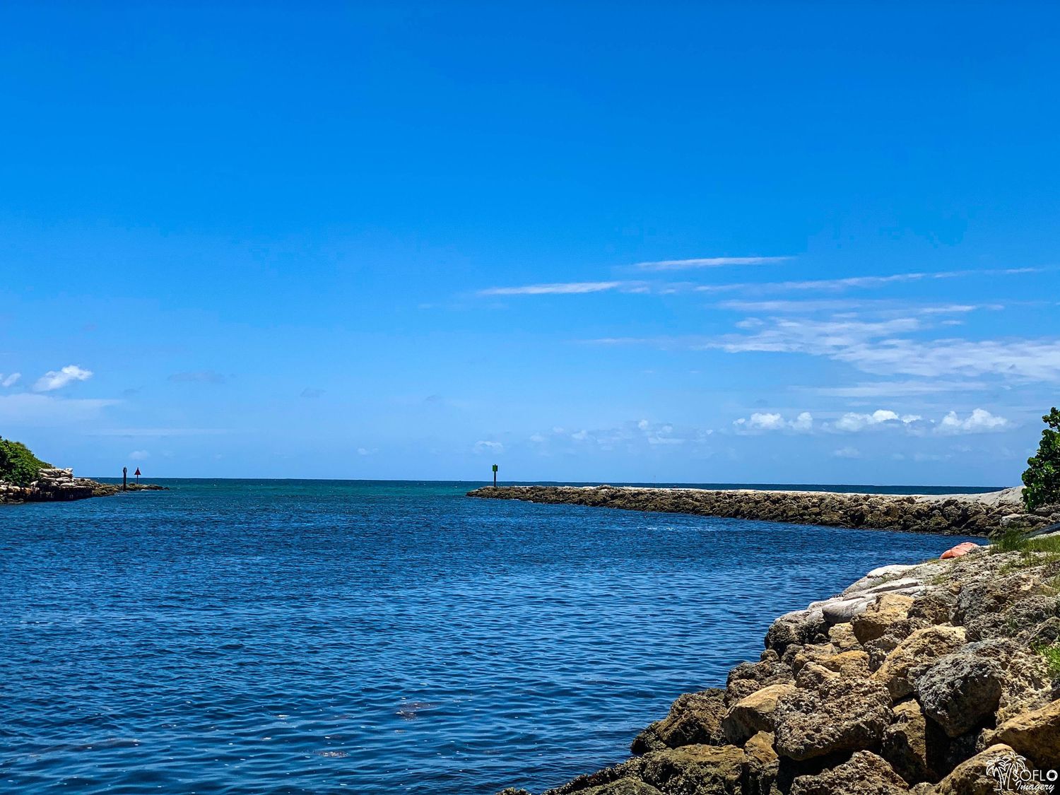 Panoramic seascape showing a rocky coastline and lighthouse under bright blue skies.