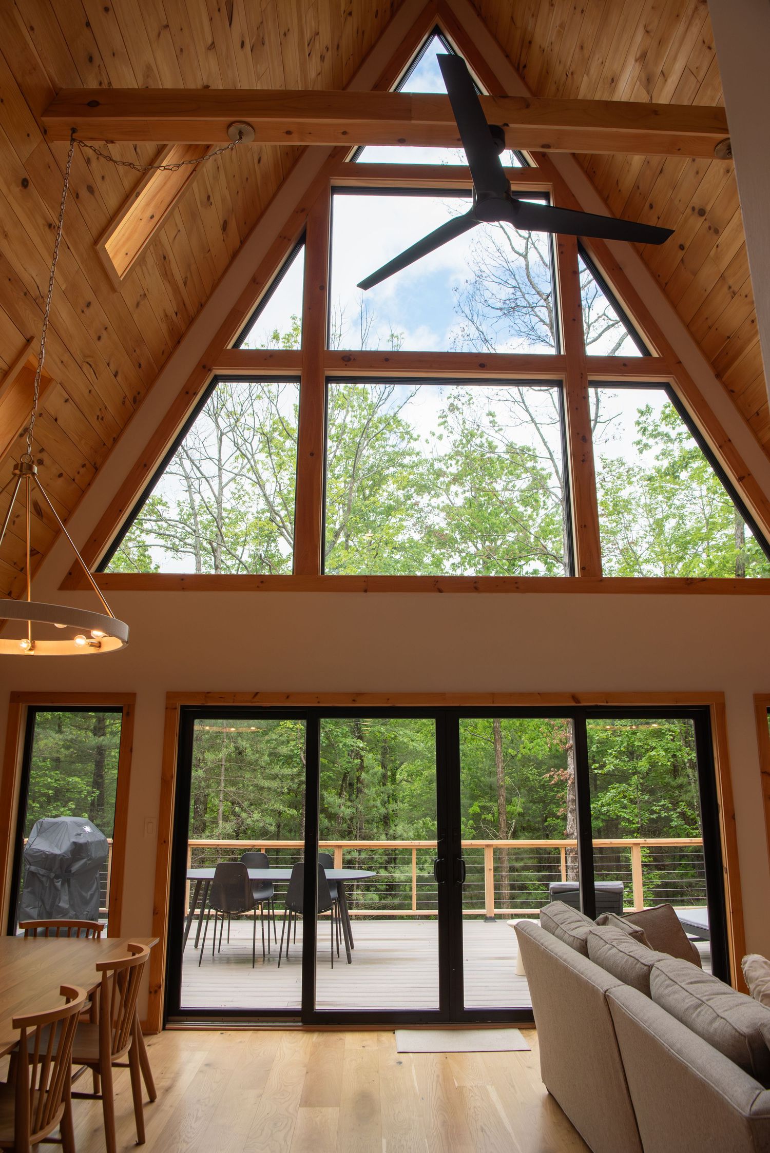 A-frame living room with high wooden ceilings and floor-to-ceiling windows overlooking forest views.