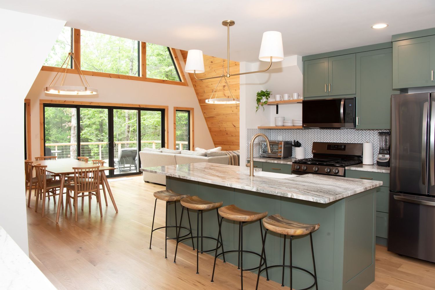 Open concept living space with sage green kitchen cabinets and large windows bringing in natural light.