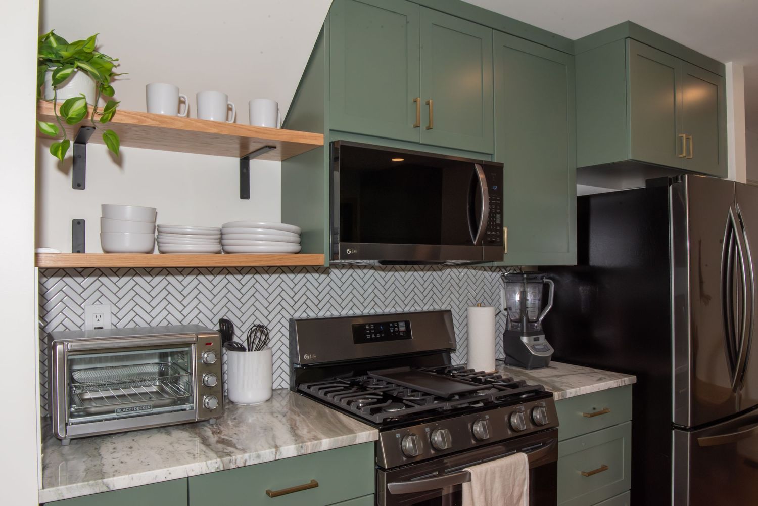 Elegant kitchen renovation with green cabinets, stainless appliances, and white marble backsplash.