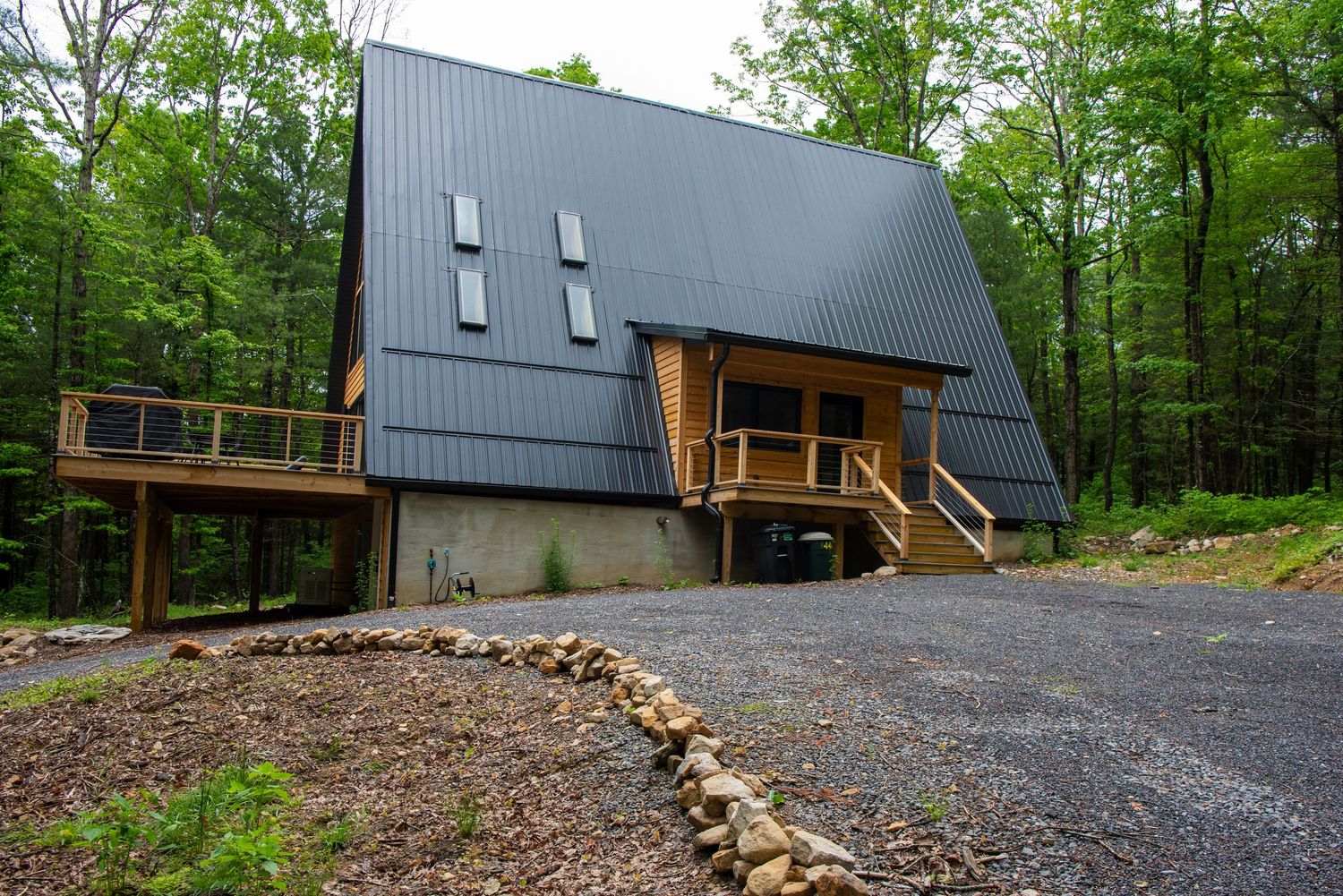 Contemporary A-frame house with grey metal roof and wooden accents surrounded by trees.