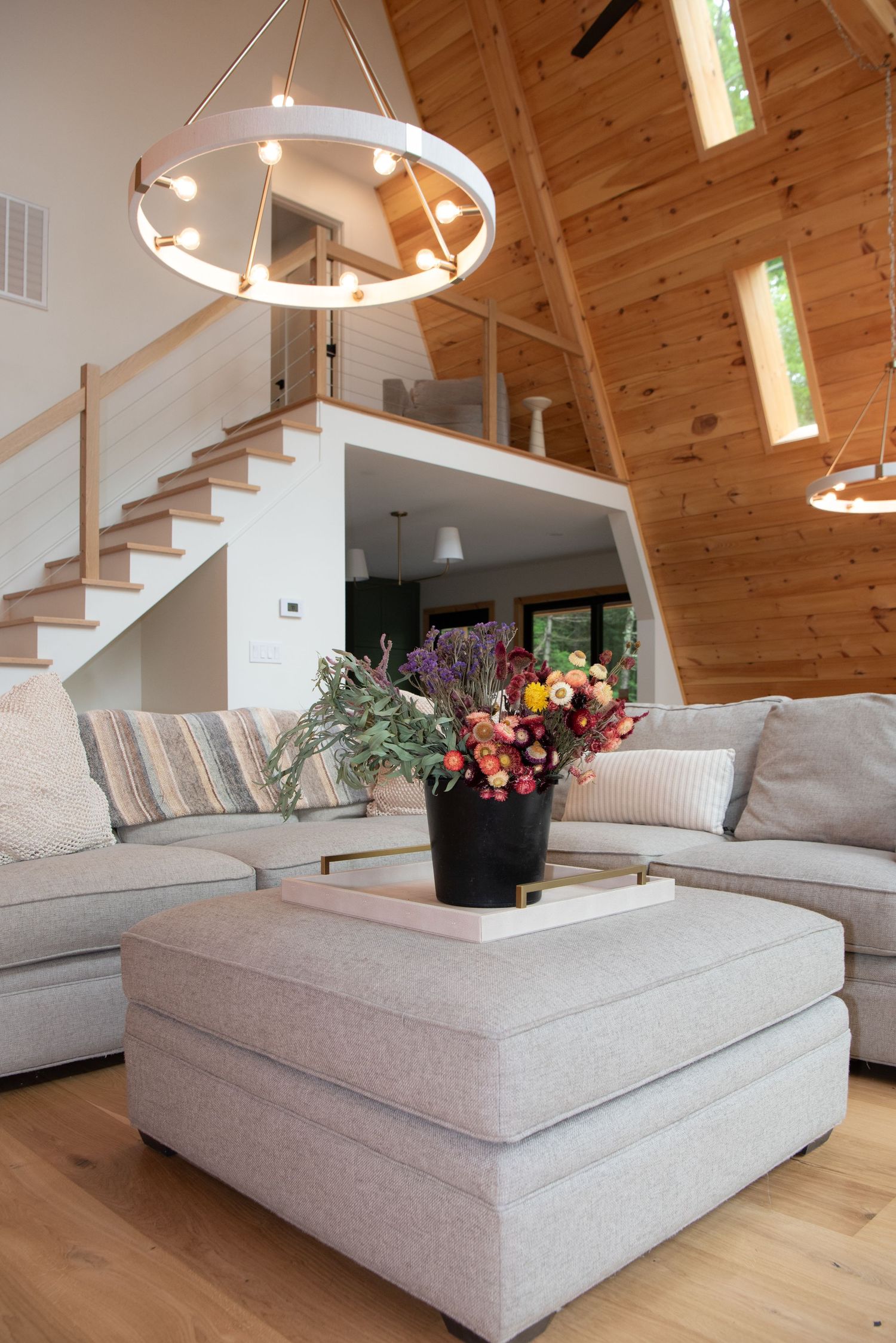 Modern living room with circular chandelier, sectional sofa and floral arrangement on ottoman.
