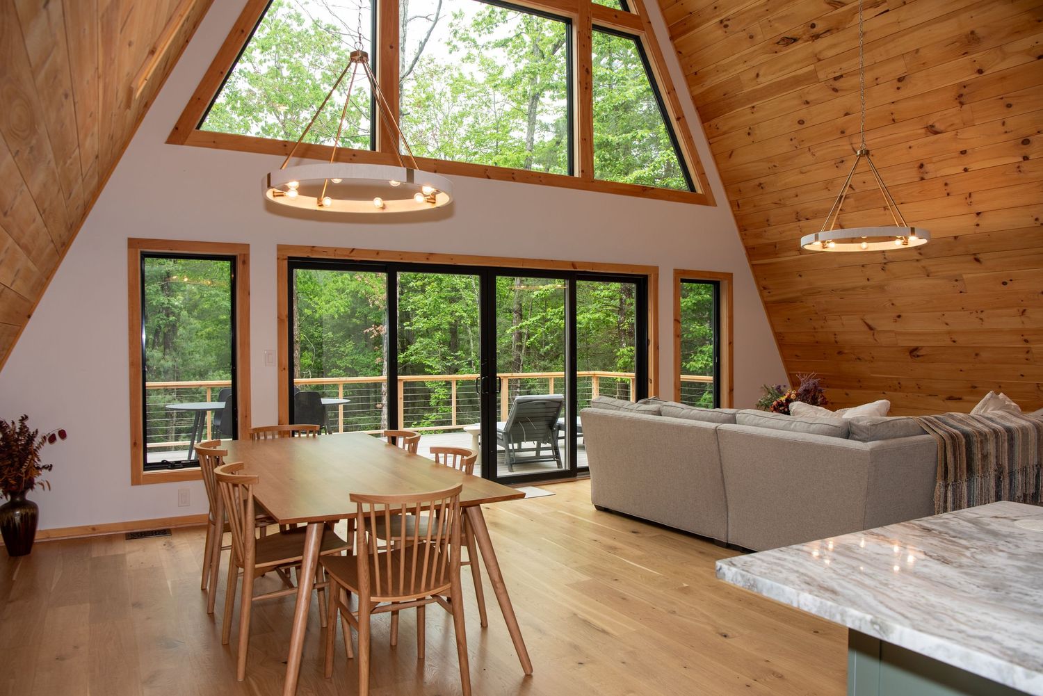 A-frame cabin interior with large windows, wooden ceiling, and open concept dining and living space.