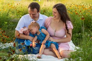 Family sits on blanket in wildflower field during summer photoshoot.