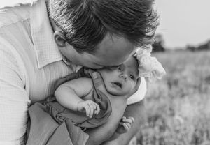 Intimate black and white portrait of parent embracing baby in field.