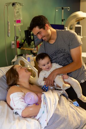 A tender moment in a hospital room as a family welcomes their newborn baby while medical equipment surrounds them.