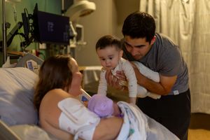 Parents sharing an intimate moment with their newborn in a hospital bed surrounded by medical equipment.