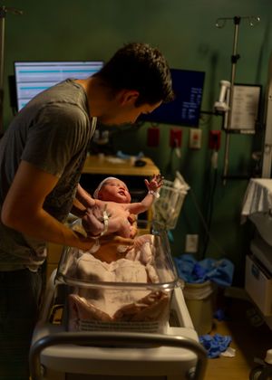 A newborn baby receives care in a hospital bassinet while being attended to by medical staff.
