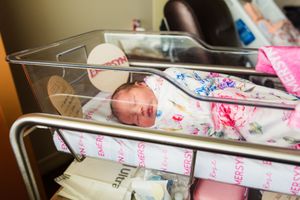 Newborn baby swaddled in floral blanket sleeping peacefully in hospital bassinet after birth.
