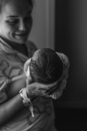 Black and white photo of a smiling mother holding her newborn baby, capturing a tender moment of new parenthood.