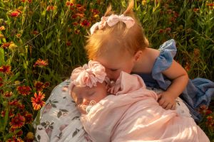 Two siblings share a tender moment on a blanket among blooming wildflowers at sunset.