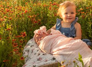 A child sits on a floral blanket surrounded by vibrant red wildflowers in a meadow.