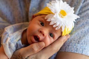 Baby wearing yellow and white flower headband smiles brightly.