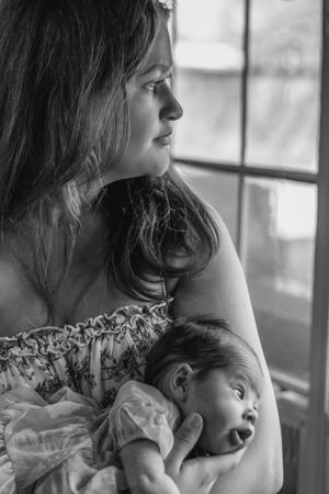 Mother and sleeping baby share tender moment by window in black and white portrait.