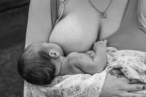 Black and white image of a nursing baby swaddled in soft fabric.