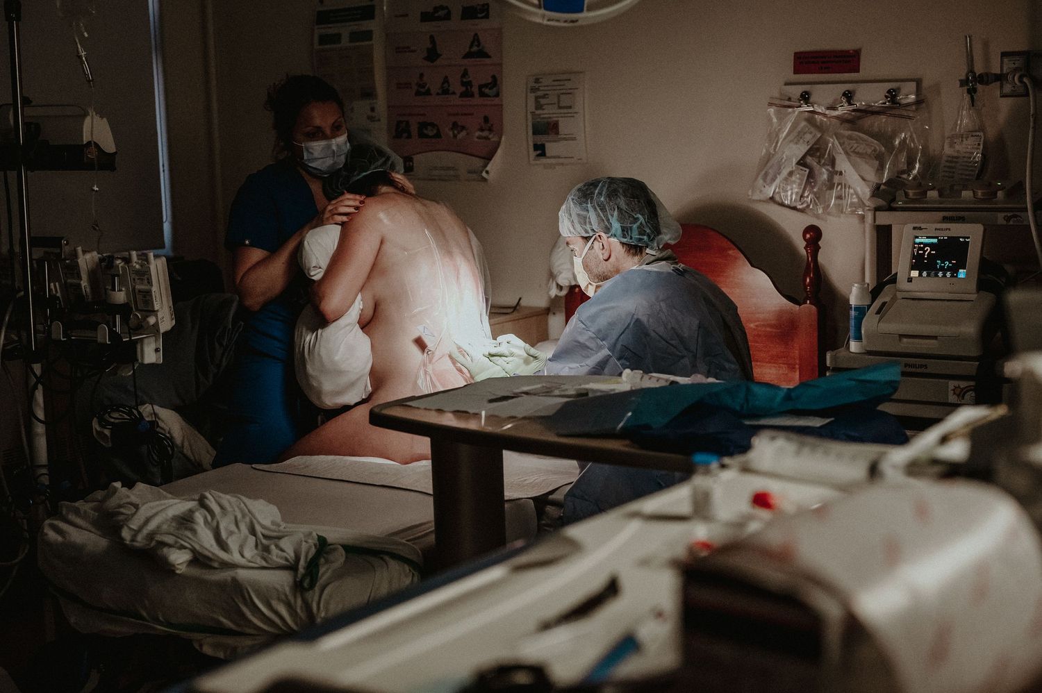 Medical professionals work intently in a dimly lit hospital room with medical equipment visible in the background.